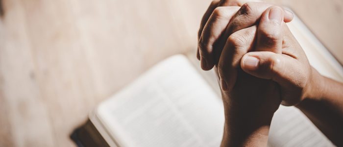 spirituality and religion, hands folded in prayer on a holy bibl
